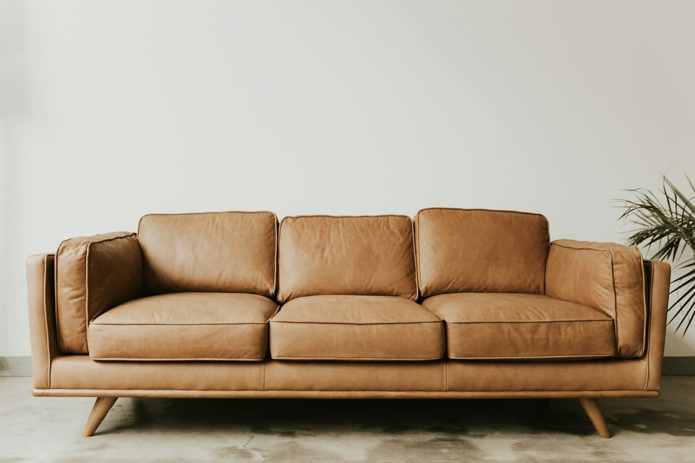Three-seat tan leather sofa with tapered oak legs